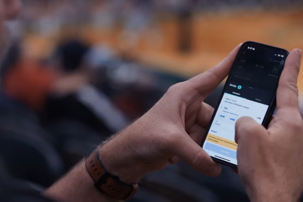 Ruka osobe drži pametni telefon i koristi aplikaciju dok sedi u gledalištu sa zamućenom pozadinom