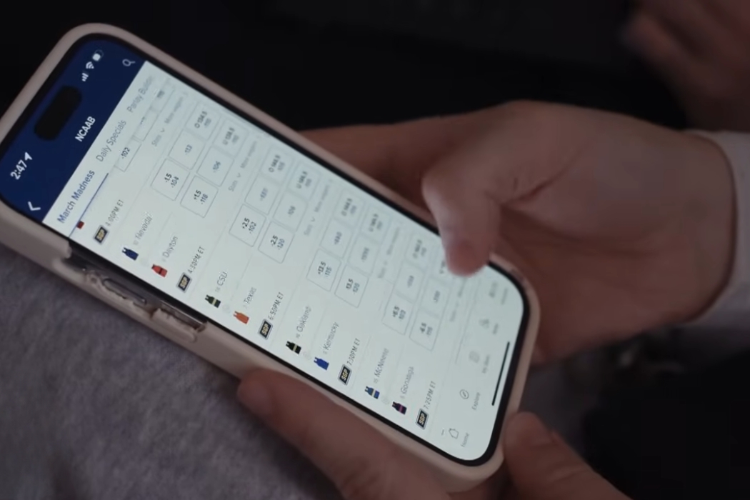 Osoba drži telefon i pregledava kvote za sportsko klađenje na ekranu