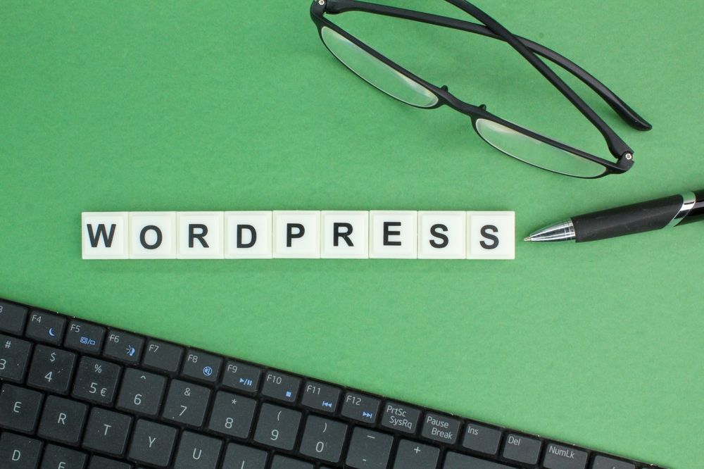Natpis WordPress pored tastature, naočara i olovke na radnom stolu.