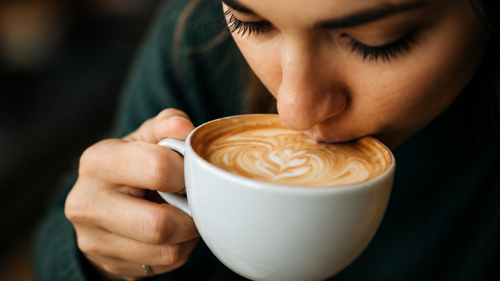 Osoba uživa u šolji kafe sa latte art penom u prijatnom ambijentu kafića