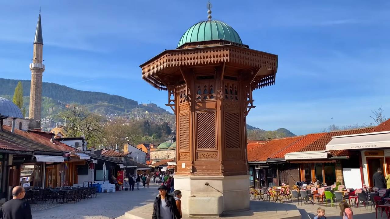 Sebilj na Baščaršiji u Sarajevu, okružen tradicionalnim radnjama, kafićima i prolaznicima.